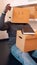 Vertical, happy young man with cardboard box on the head performing hand dance in the new apartment