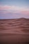 Vertical high-angle view of a caravan of camels in the sand dunes under the cloudy sunset sky