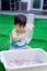 Vertical image. Asian baby boy playing colorful water beads. Child pouring rainbow beads from bottle to white basin.