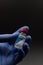 Vertical image of a blue gloved hand holding a COVID vaccine vial on dark background