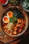 vertical image of closeup bowl of delicious ramen on a wooden table, tasty traditional asian noodle soup top view