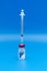 Vertical image of a COVID-19 vaccine vial with a syringe inserted into it upright on a blue background