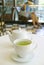 Vertical image of a cup of green tea and teapot on white table in a cafe