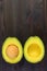 Vertical image of cut in half fresh ripe avocado isolated on black wooden background