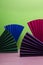 Vertical image.Different colors of papaer fan on the pink surface against green background.Empty space