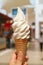 Vertical Image of a female`s hand holding vanilla milk soft serve ice cream cone on a sunny day