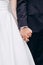Vertical image of a groom in a blue suit holding the bride`s hand tightly. Wedding details.