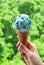 Vertical Image of Hand holding Mint Choc Chip Ice Cream in Cone against Blurry Sunshine Garden