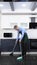 A vertical image. handsome man in tie and apron sweeping the kitchen floor