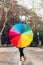 Vertical image of a modern woman showing her colorful umbrella to the camera. Impersonal photo of urban life on a windy and rainy
