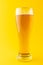 Vertical image of nearly full pint glass of lager beer on yellow background, with copy space