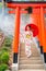 Vertical image of pretty woman with Japanese style dress hold red umbrella and stand on stair with red arched entrance and look to