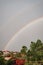 Vertical image of a rainbow above a village with trees and against a hazy sky