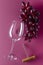 Vertical image of red grapes, glasswine and handle corkscrew on the pink surface