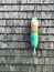 Vertical image of a single colorful lobster buoy against a wooden shingled background in Maine, USA