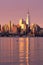 Vertical image of the skyline of Lower Manhattan at sunrise, with reflections seen in the Hudson River.