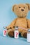 Vertical image of teddy bear with unnamed vial dose of vaccine or another medicine with syringe against blue background with copy