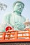 Vertical image of two Asian pretty women stay close to red railing in the area of base of green big buddha statue and they look