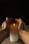 Vertical image.Warm candle flame, white cylindrical candle and human hands against drk background.Empty space