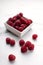 Vertical image. White bowl full of rasberries on the white marble table