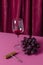 Vertical image of wineglass of red wine, corckscrew and grape on the dark pink table against folds of curtain