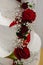 Vertical images of beautiful modern white wedding cake decorated with fresh red roses.