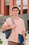 Vertical individual portrait of a handsome student young man standing at university campus. Happy teenage male smiling