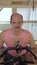 Vertical, medium shot, funny bald man is training on an exercise bike, smiling