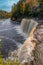 Vertical of the mesmerizing Tahquamenon Falls waterfall in Michigan surrounded by autumn foliage