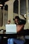 Vertical multicultural dark skin woman drink coffee and work using laptop to analyze data in cafe. Point index finger up