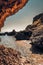 Vertical of ocean waves approaching a coastal cave and rock formations under sunlight