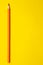 Vertical orange sharp wooden pencil on a bright yellow background, isolated, copy space, mock up