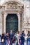 Vertical of people on the Piazza del Duomo passing in front of the central bronze door to the cathedral.