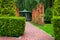 Vertical pergola made of brown wood in a roses garden with a stone tile walkway.