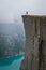 Vertical photo 0f tourist standing at Prekestolen rock\'s edge.