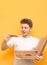 Vertical photo of amazed guy on a yellow background, with a box and a piece of pizza in his hands, looks with a hungry look. Fast