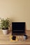 Vertical photo angle view to workspace desk. Laptop with blank screen, potted plant, mug, yellow notepad, pen, mobile phone and