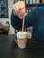 Vertical photo behind the bar counter with blurred background and soft focus. Hand of a person mixing morning coffee