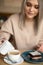 Vertical photo of blurred blond smiling woman pouring milk cream in coffee, eating brownie cake. Cafe holiday pleasure