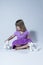 Vertical photo of cute little girl in mauve top and purple skirt sitting cross-legged