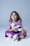 Vertical photo of cute little girl in mauve top and purple skirt sitting cross-legged