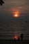 Vertical photo of Dramatic red sunset, Sun behind foggy clouds, silhouettes of children, man and women at seashore line