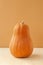 Vertical photo elongated orange oval pumpkin of the Matilda variety on a monochrome beige background, food minimalism trend,