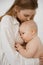 Vertical photo of kissing blond gentle woman with bare chest, holding little hungry baby eating, breastfeeding, asleep