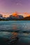 Vertical photo of a lake with some rocky snowy peaks of a mountain with the sun coming out behind