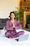 Vertical photo of a middle aged woman yoga practicing in bed in front of laptop monitor.