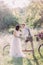 The vertical photo of the newlyweds in the sunny forest. The bride in the white dress is petting the shoulder of the