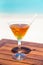 Vertical photo of the orange color cocktail with paper straw on the wooden table at the beach and ocean