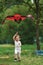 Vertical photo. Positive female child running with red and black colored kite in hands outdoors