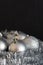 Vertical photo of shiny and bright silver christmas balls decoration lying on silver christmas chain on dark black structured